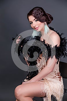 Brunette  beautiful woman in boa from ostrich feathers sit on the chair.  20`s years