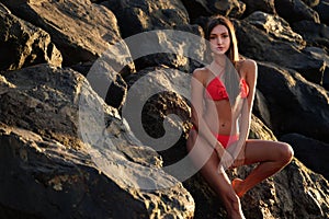 Brunette beautiful woman in red fashionable bikini posing on rocky beach