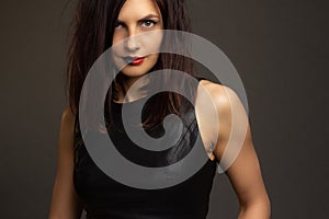 A brunette in a black leather sleeveless blouse poses on a gray background