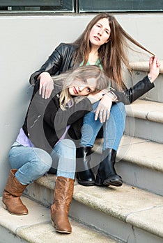 Brunette and blonde girls sitting on stairs in an urban environment