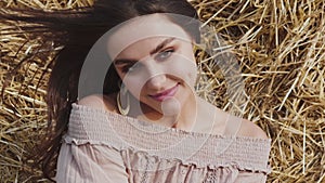 Brunette with blowing hair laughing gently and looking into camera at hay