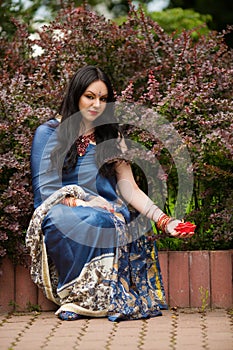 Brunette in blue sari sits near barberry bushes photo