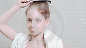 Brunette boy combing wet hair near the mirror. White towel around the neck.