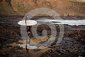 Brunette boy standing with a surf in his hands on the rock beach