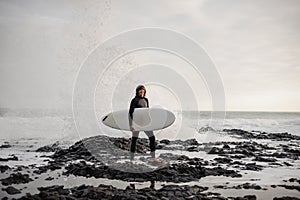 Brunette boy standing with a surf in his hands on the shore on the day