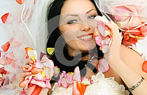 Brunette bride on the bed covered with rose leaves