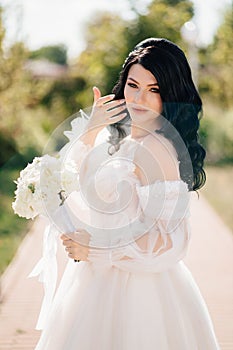 brunette bride in a dress with a bouquet of flowers on the path in the park.