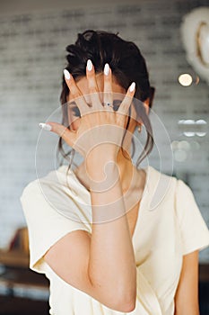 Brunette bride showing hand with wedding ring and hiding face.