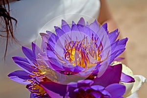 A brunette bride in a wedding dress holding a bouquet of purple lotuses. Wedding rings in lotus buds