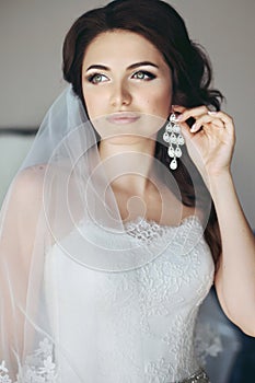 brunette bride in white dress putting on earring