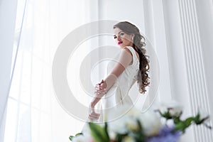 Brunette caucasian bride in wedding dress at window flowers