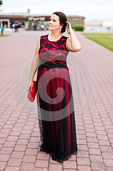 Brunette caucasian model in floor-length black and red dress corrects hair on street