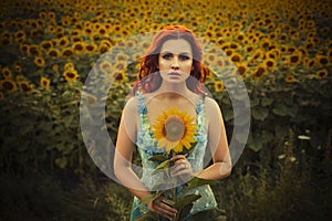 Brunette caucasian woman in blue dress at the park in flowers on a summer sunset holding sunflowers