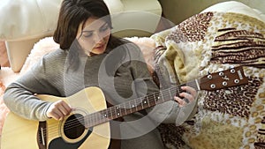 Brunette in a chair fingering the strings of the guitar