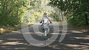 Brunette charming woman is cycling on bicycle in sunny green park. Beautiful young girl rides vintage retro bike in forest in summ