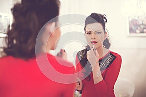 Brunette with curly hair in a red dress colors her lips in the mirror
