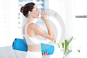 Brunette drinking water while holding exercise mat