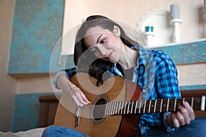 Brunette eastern woman sitting on her bed in the bedroom holding guitar composing a song - musician, songwriter, composer concept