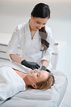 Brunette esthetician makes beauty injections to a blonde woman