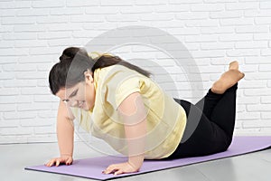 Brunette fat girl is trying to do push ups in mat indoors