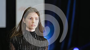 Brunette female model walk on podium. Girl in black dress with fringe pattern.