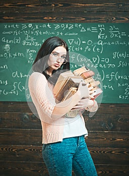 Brunette female student in classroom. young college girl walking with two heaps of books