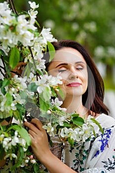 Brunette in flowers. The girl hugs a large bouquet of white flowers and smiles with her eyes closed. A young woman in flowers with