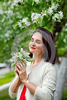 Brunette in flowers. The girl hugs a large bouquet of white flowers and smiles with her eyes closed. A young woman in flowers with