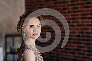 A brunette girl in a beautiful dress posing against a background of an authentic brick wall