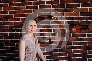 A brunette girl in a beautiful dress posing against a background of an authentic brick wall