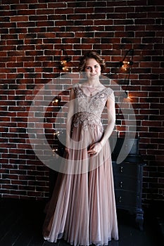 A brunette girl in a beautiful dress posing against a background of an authentic brick wall