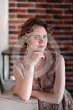 A brunette girl in a beautiful dress posing against a background of an authentic brick wall