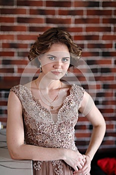 A brunette girl in a beautiful dress posing against a background of an authentic brick wall