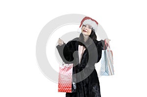 Brunette girl in black fur coat in santa hat with shopping bags on isolated background, christmas shopping, sale santa claus