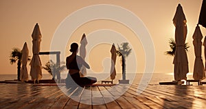 A brunette girl in a black sports summer uniform sits on a carpet on the beach, which is covered with boards, and