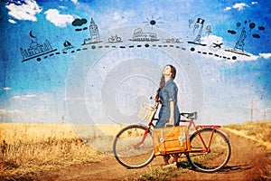 Brunette girl with bycicle and suitcase on country side road.