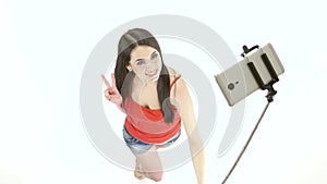 Brunette girl doing selfie photos using a monopod. White background