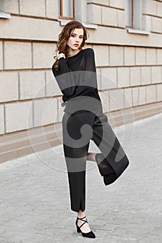 Brunette girl dressed in black blouse and trousers poses in the city street on a sunny day