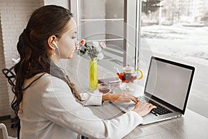 Brunette girl with earphones listens and typing on laptop.