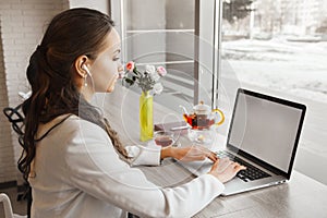 Brunette girl with earphones listens and typing on laptop. photo