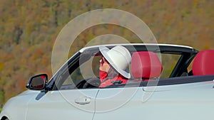 Brunette girl enjoys mountains view from convertible car in her road trip.