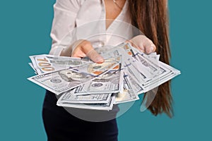 Brunette girl in glasses, wearing in a black short skirt and white blouse is posing holding a fan of hundred dollar