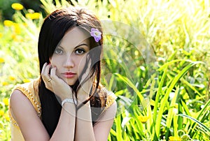 Brunette girl on green grass at summer park. Portrait of young beautiful woman