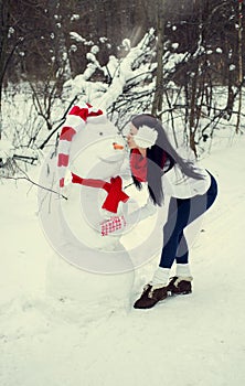 Brunette girl in hat and mittens sculpts a snowman