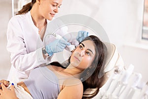 Brunette girl having facial beauty massage by European female aesthetician & x28;vabration import& x29;