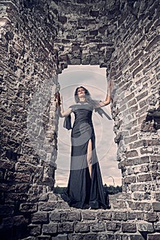 A brunette girl with long hair in an evening dress in a vintage Gothic castle. A woman who looks like an evil witch or