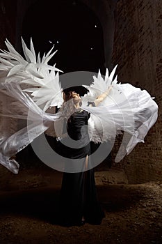 A brunette girl with long hair and white wings in an evening dress in a vintage Gothic castle. Woman who looks like an