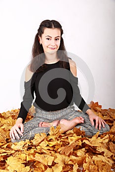 Brunette girl lying in lotus yoga pose on autumn leaves