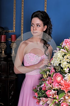 Brunette girl in a pink elegant dress among the flowers in the room