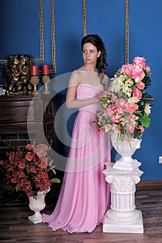 Brunette girl in a pink elegant dress among the flowers in the room